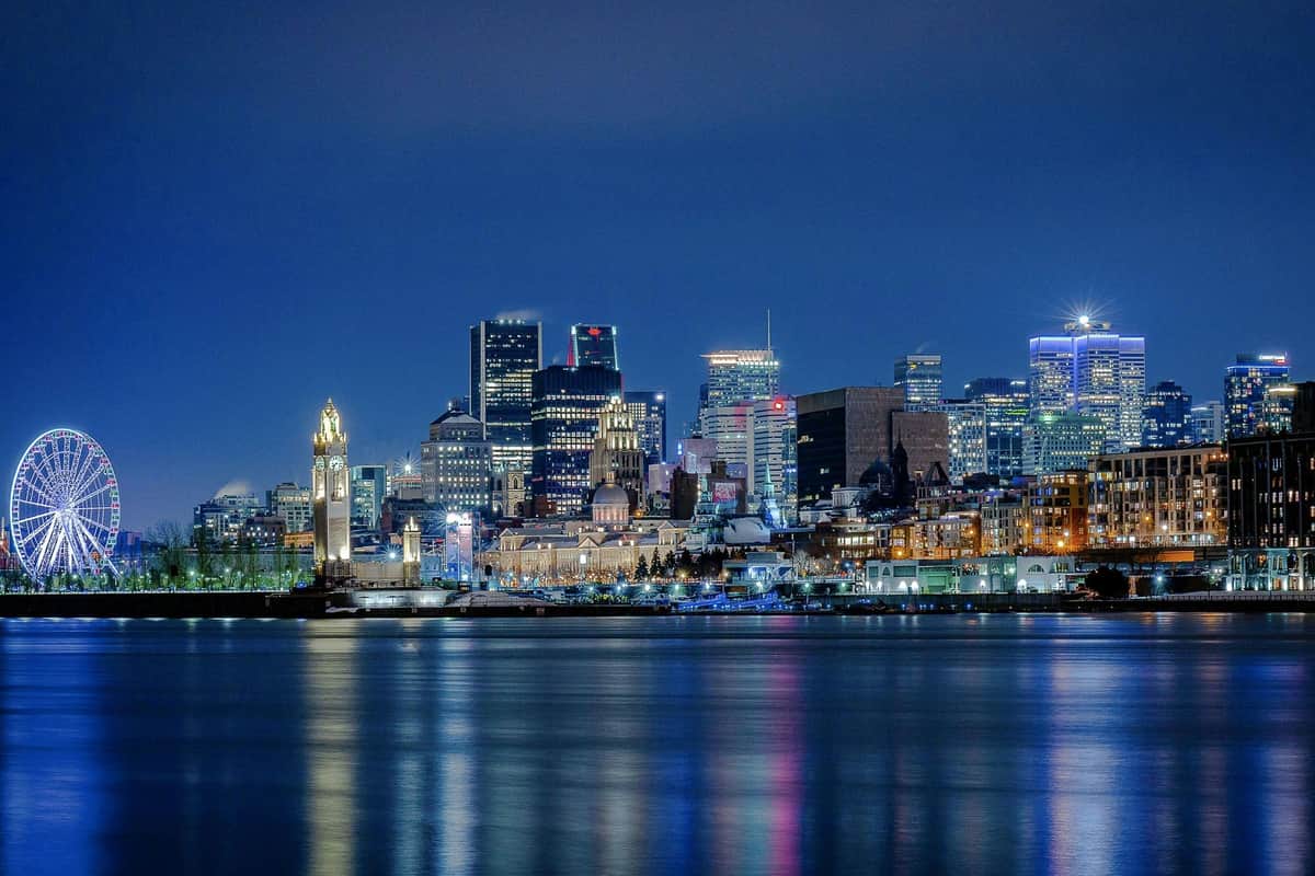 Montreal Guided Evening River Cruise City skyline at night with illuminated buildings reflecting on a calm body of water.