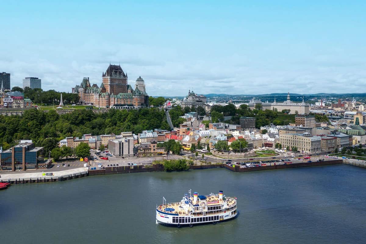 Quebec City: Guided Sightseeing River Cruise A scenic view of Quebec City with Château Frontenac on the hill, colorful buildings below, and a ferry on the river in the foreground.