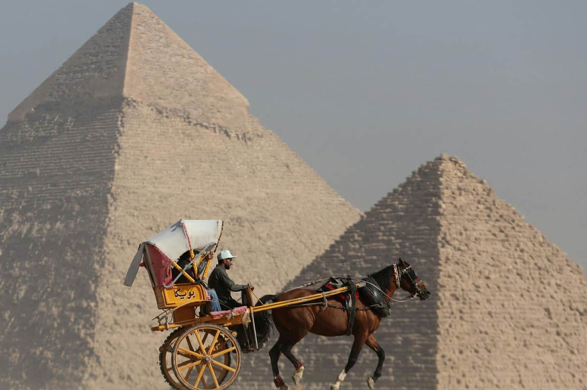 Pyramides de Gizeh et Sphinx : visite guidée + transfert + déjeuner + promenade en felouque sur le Nil Une personne en calèche devant les pyramides de Gizeh par ciel dégagé.