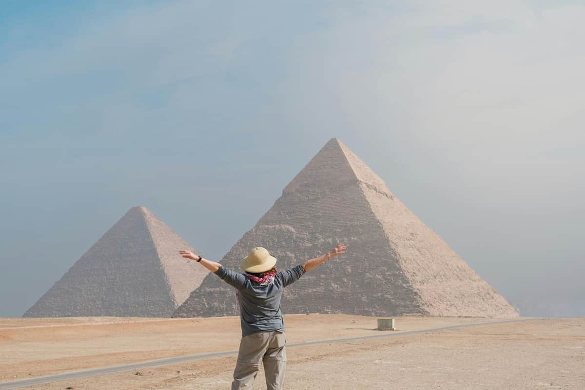 Visite des pyramides de Gizeh & du Sphinx + croisière en felouque sur le Nil Personne avec les bras tendus face aux pyramides de Gizeh par temps clair.