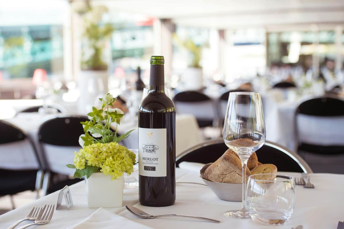 Déjeuner-croisière sur la Saône par Les Bateaux Lyonnais Hermès Une table à manger avec une bouteille de vin Merlot, un verre, du pain dans un bol et des ustensiles de cuisine dans un restaurant élégant.