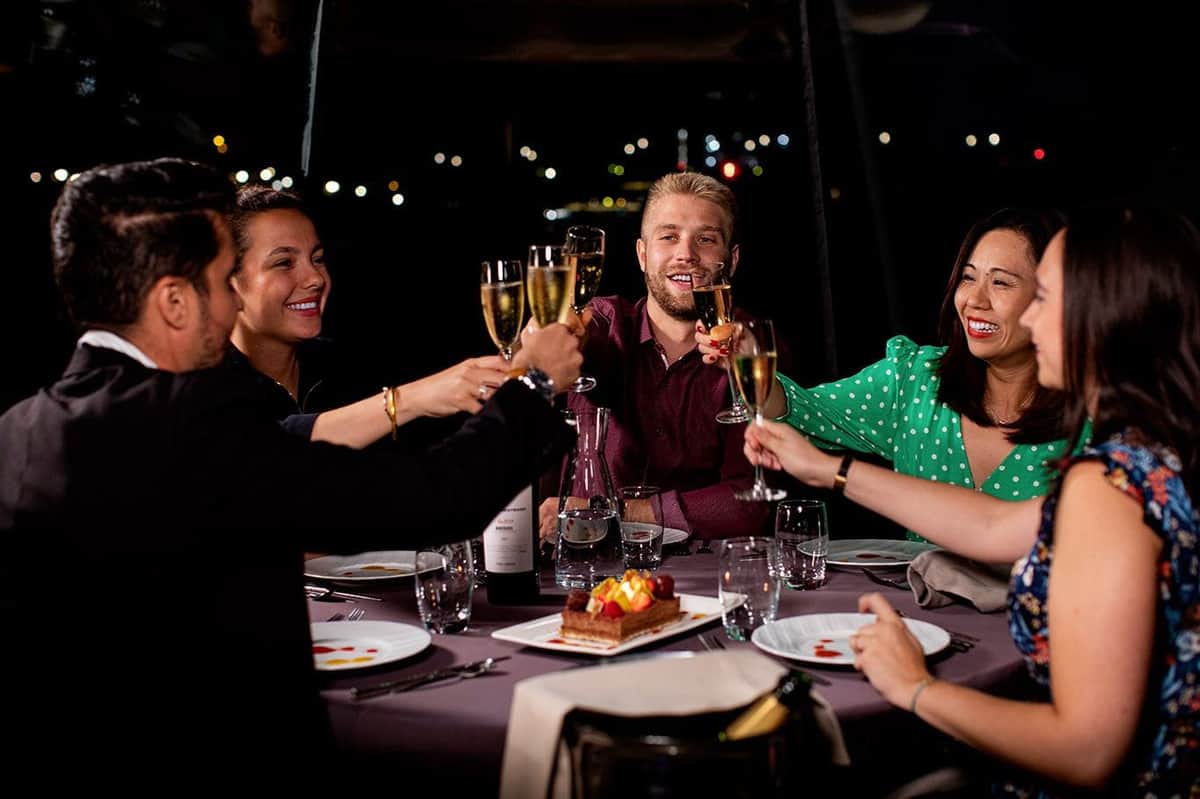 Seine River: Dinner Cruise by Bateaux Parisiens A group of five people toasting with champagne glasses around a table with desserts at an evening gathering.