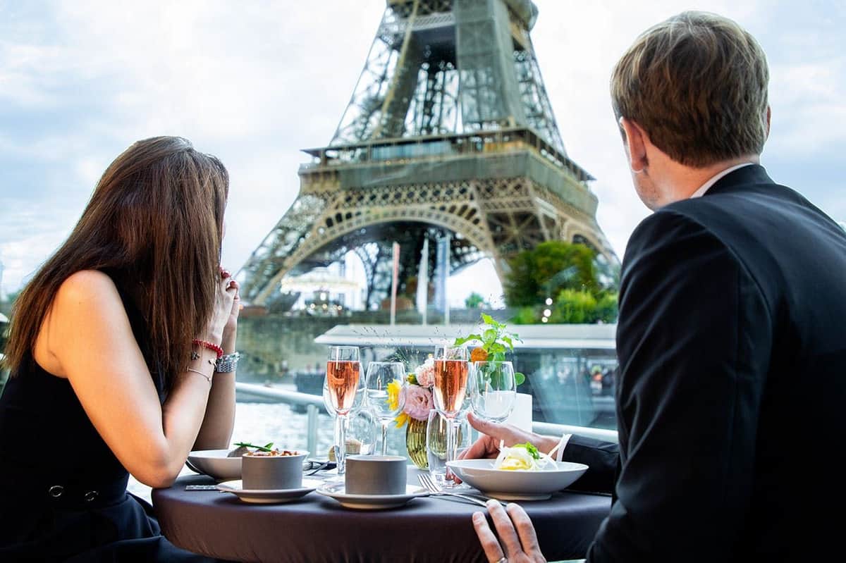 La Seine : Dîner-croisière Un couple dînant dans un restaurant en plein air avec une vue sur la Tour Eiffel en arrière-plan.