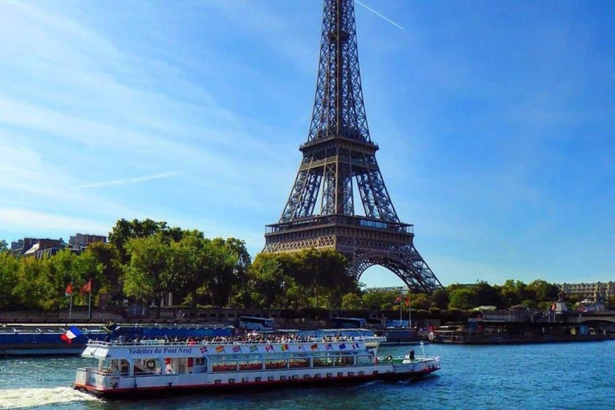Seine River: Guided Sightseeing Cruise by Vedettes du Pont Neuf A sightseeing boat on a river in front of the Eiffel Tower on a sunny day with trees and blue sky in the background.
