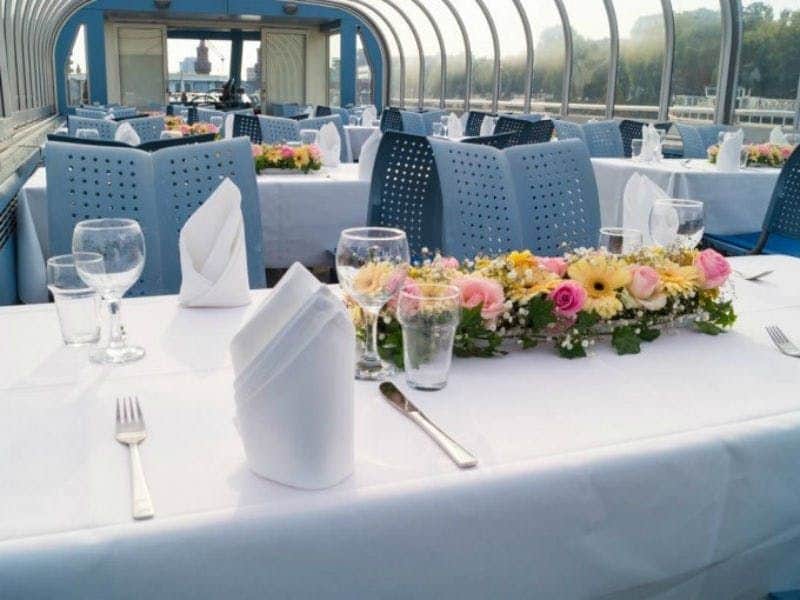 Berlin: 2.5-Hr Dinner Cruise on the MS Der Fliegende Holländer + Audio Guide Elegantly set tables with white tablecloths, folded napkins, flower centerpieces, and glassware in a glass-enclosed dining area.