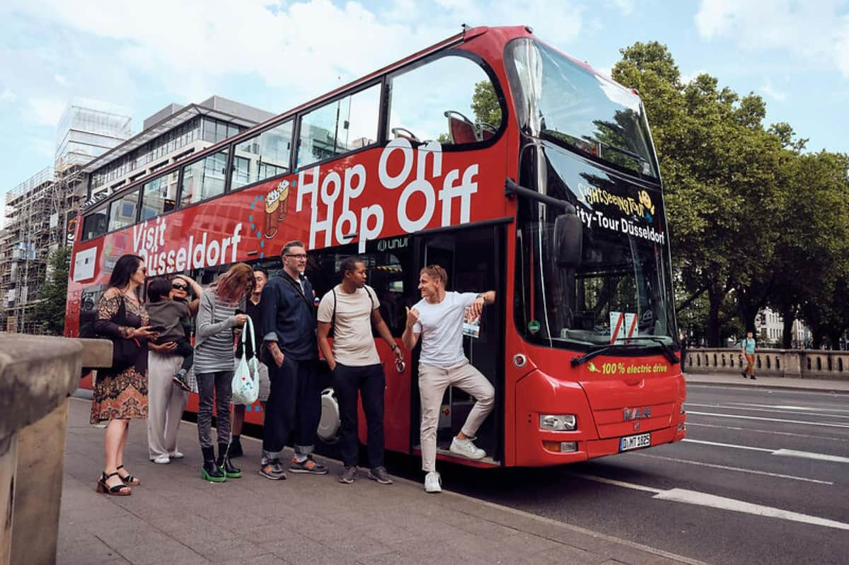 DüsseldorfCard Plus: 48, 72, or 96-Hr Public Transport A group of people standing near a red double-decker sightseeing bus with "Hop On Hop Off" written on its side.
