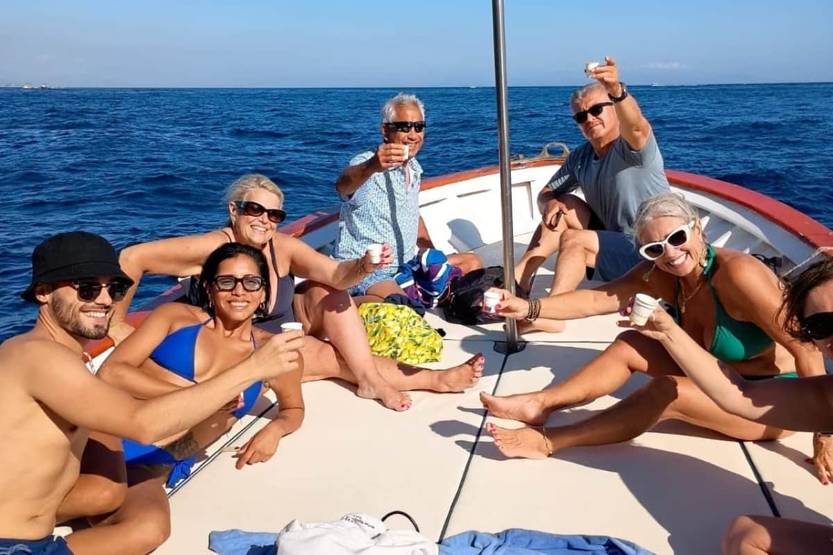 Capri: Hidden Swim Spots Private Boat Tour A group of people on a boat enjoying drinks, with the ocean and blue sky in the background.