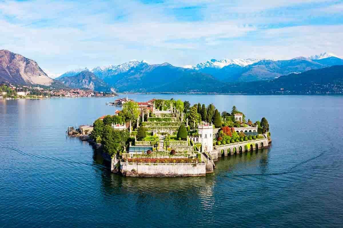 Isola Bella en bateau Jardin luxuriant en terrasses sur une petite île entourée d'un lac, adossé à des montagnes enneigées sous un ciel partiellement nuageux.