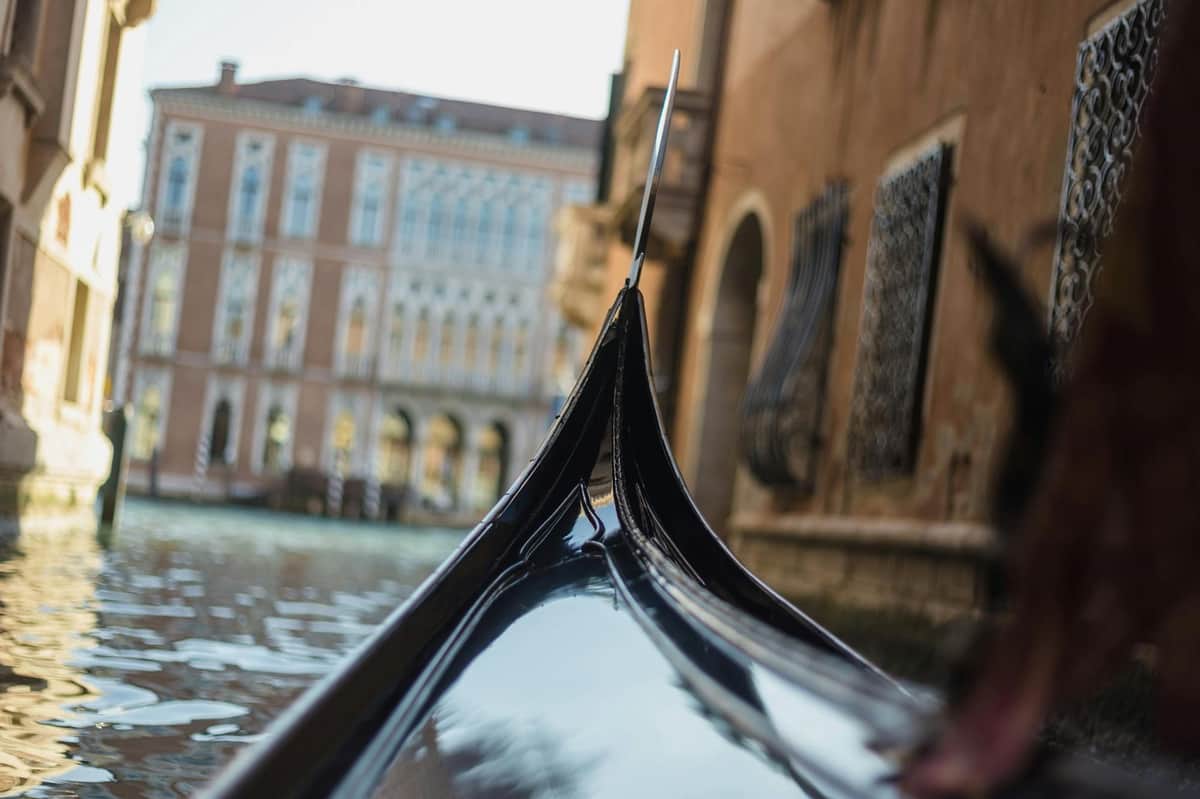 Gondola Ride & Murano, Burano Boat Tour Close-up of a gondola's prow against a canal with historic buildings and water in the background in Venice, Italy.