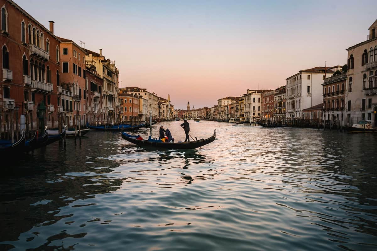 Venice: Private Gondola Ride on the Grand Canal A gondola with two people on a canal surrounded by historic buildings at sunset in Venice.