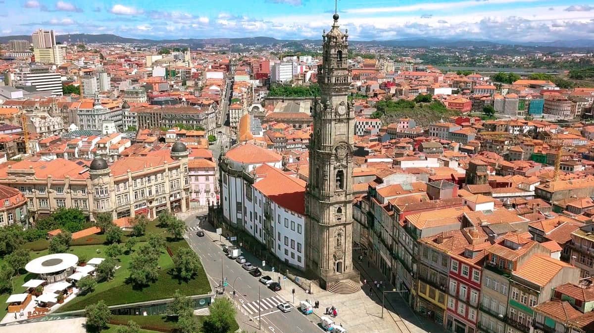 Laissez-passer pour les hauts lieux de Porto Vue aérienne d'une ville avec un grand clocher, des bâtiments aux toits rouges, des rues avec des voitures et un parc avec des arbres.