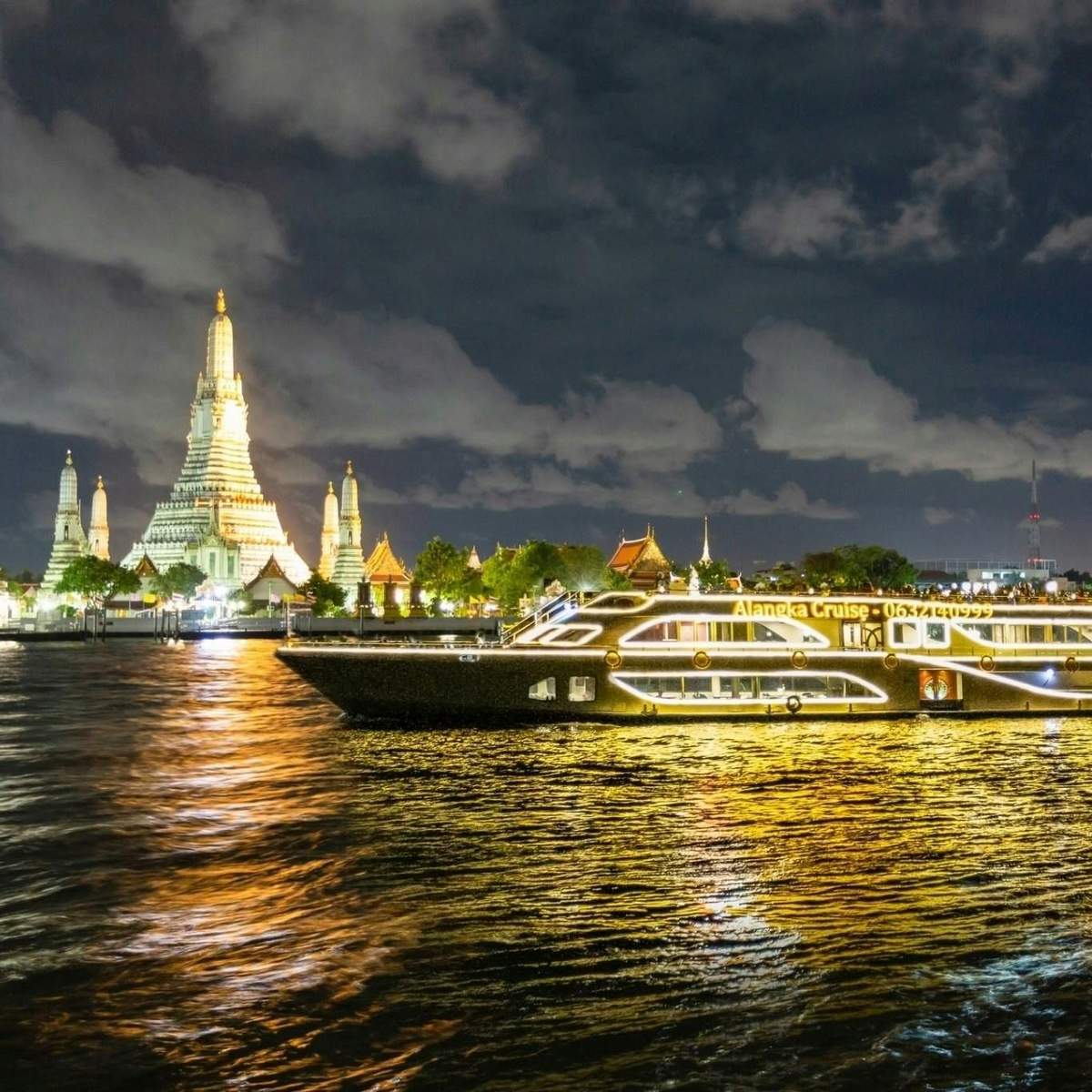 Bangkok : Dîner-croisière Alangka à l'ICONSIAM Un bateau de croisière illuminé sur un fleuve la nuit avec un grand temple illuminé et d'autres bâtiments à l'arrière-plan.