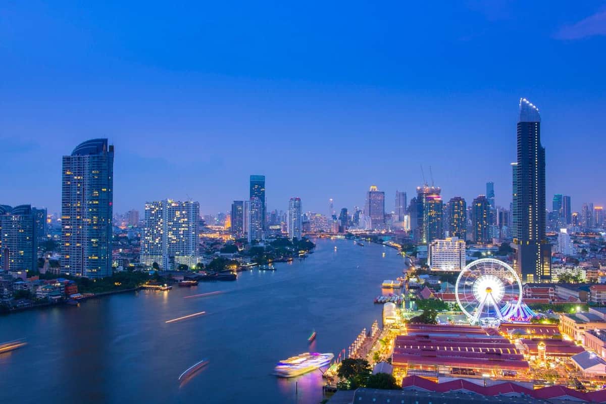 Bangkok: Meridian Dinner Cruise from INCONSIAM Cityscape at dusk featuring a river, illuminated buildings, a colorful riverfront, and a large Ferris wheel.