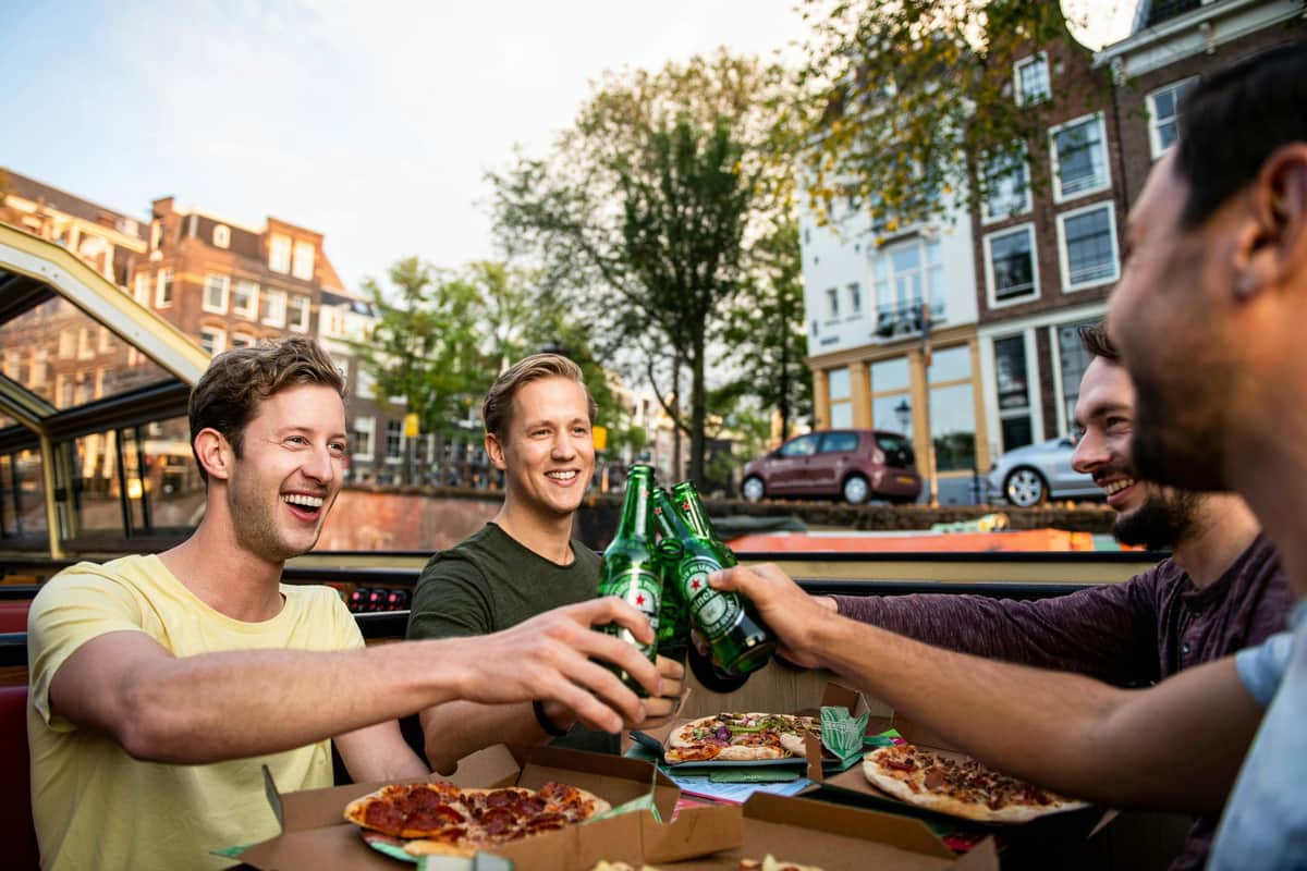 Amsterdam: Evening Canal Cruise with Pizza & Drinks Friends toast during a canal cruise through Amsterdam with pizza.