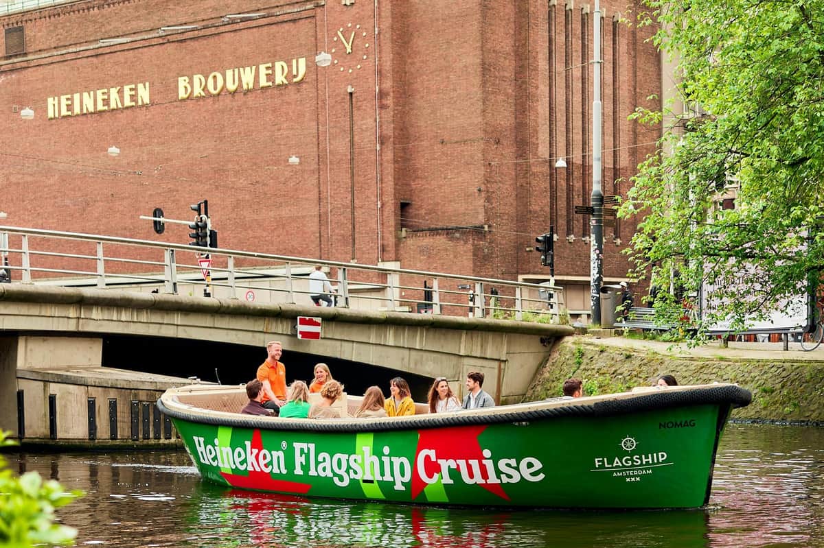 Amsterdam : Croisière Heineken Flagship Une péniche portant l'inscription « Heineken Flagship Cruise » passe sous un pont près du bâtiment de la brasserie Heineken.