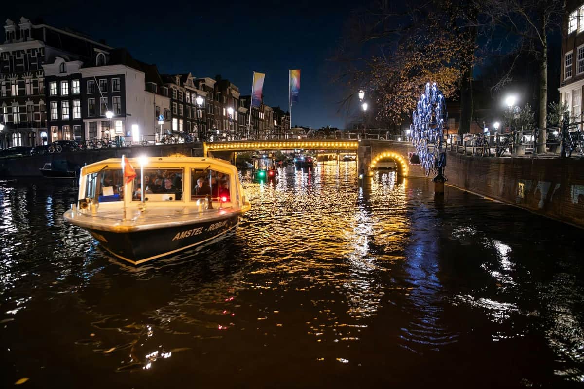 Amsterdam Light Festival: Boat Tour A canal at night with a boat, illuminated bridge, and festive lights. People are visible inside the boat.