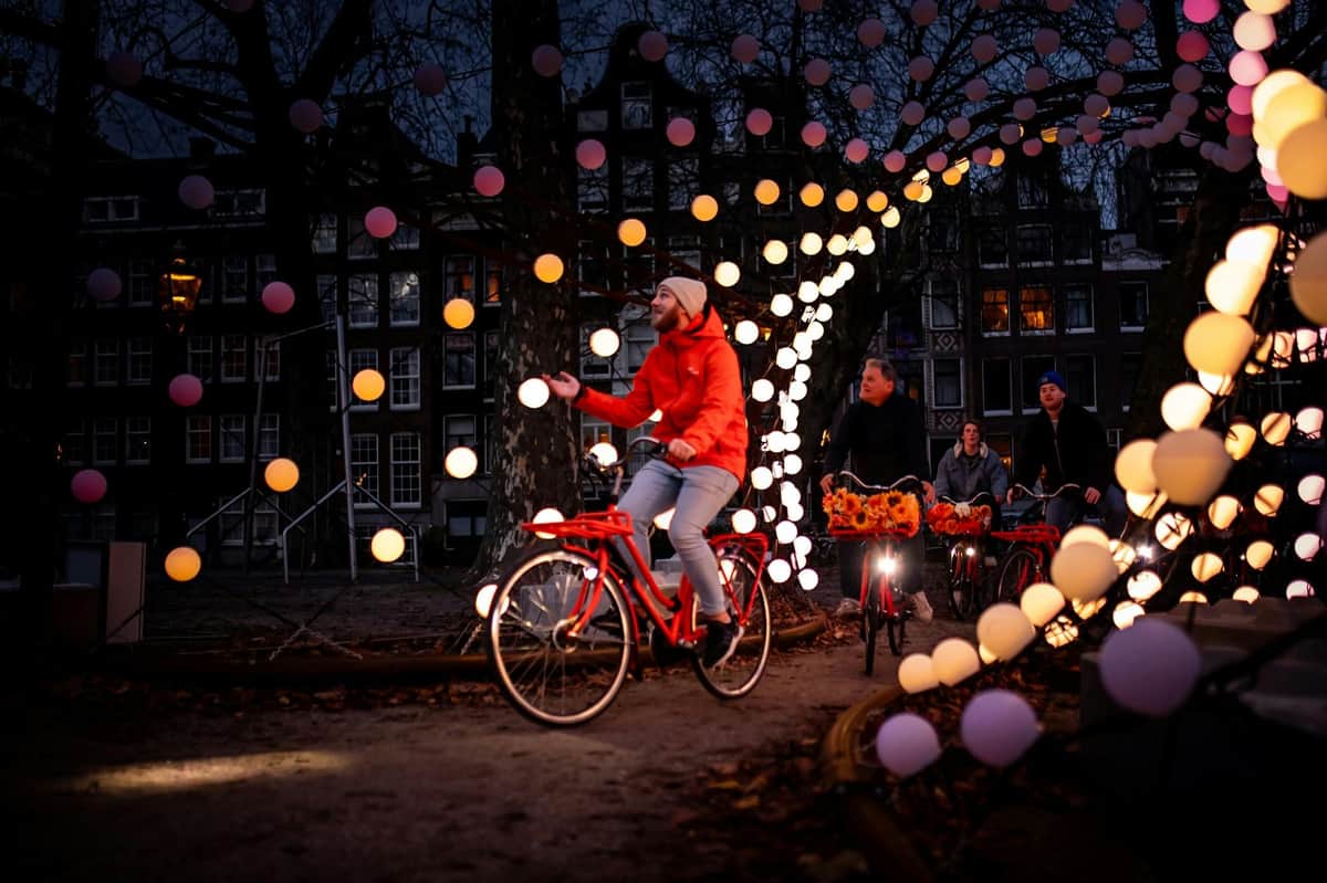 Amsterdam Light Festival: 가이드와 함께하는 자전거 투어 해질 무렵 빛나는 구형 조명으로 장식된 공원을 배경으로 자전거를 타는 사람들.