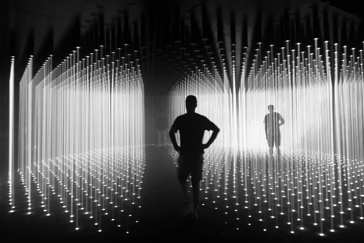 Amsterdam Noord Pass Silhouettes of people walking through a room with vertical light beams from ceiling to floor.