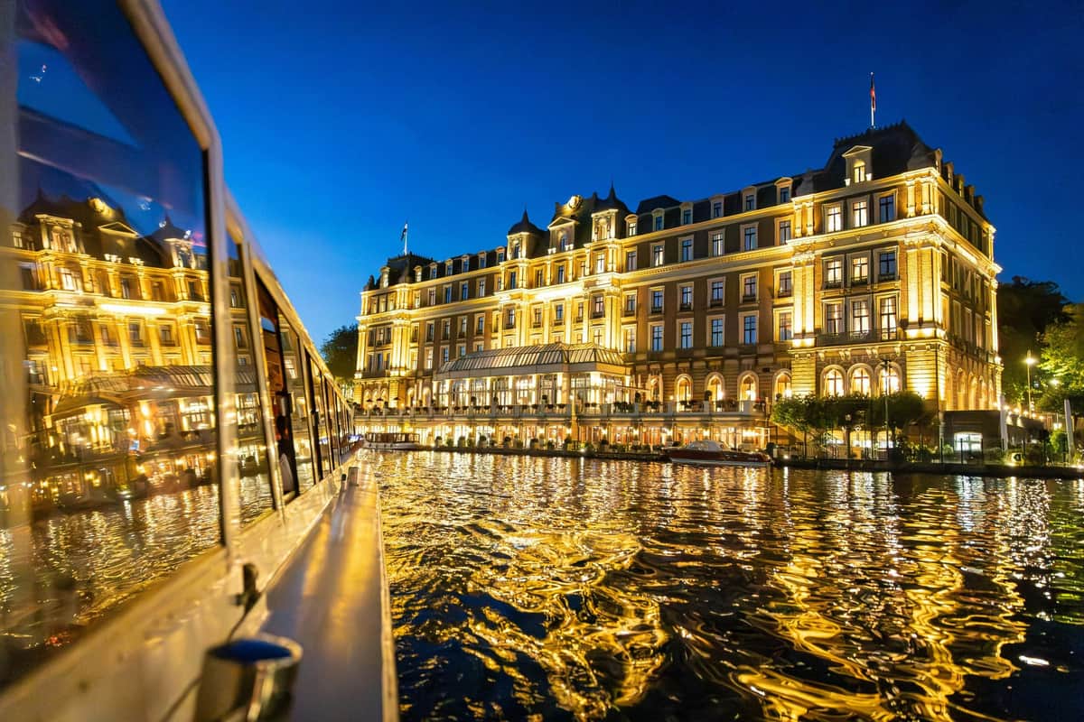 Croisière nocturne hivernale à Amsterdam Illuminated building reflecting in water at twilight, with a boat visible on the left side of the image.