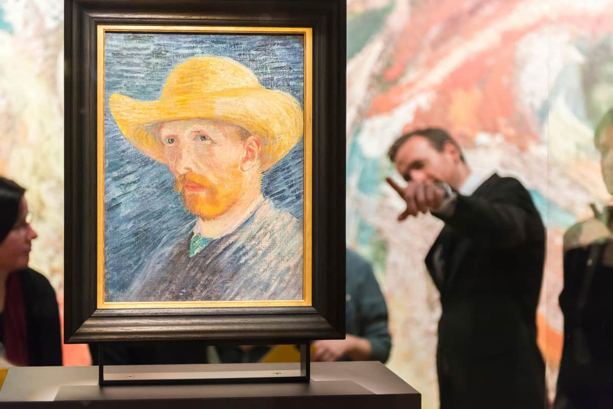 Van Gogh Museum: Entry Ticket + Canal Cruise A framed painting of a man with a yellow hat and a red beard, displayed in a gallery with two people talking in the background.