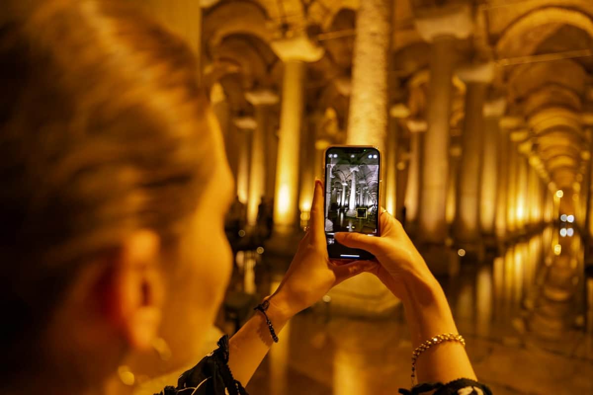 Basilica Cistern: Skip The Line Ticket & Guided Tour with Bosphorus Cruise A person is photographing an illuminated ancient columned hall with their smartphone.