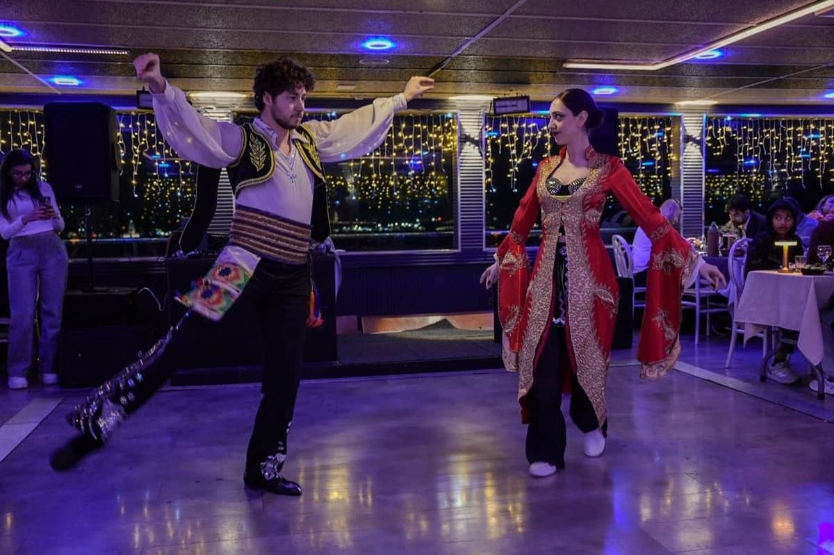 Istanbul: Bosphorus Dinner Cruise with Live Show in a Catamaran A man and a woman perform a traditional dance on a well-lit floor, with people seated at tables in the background.