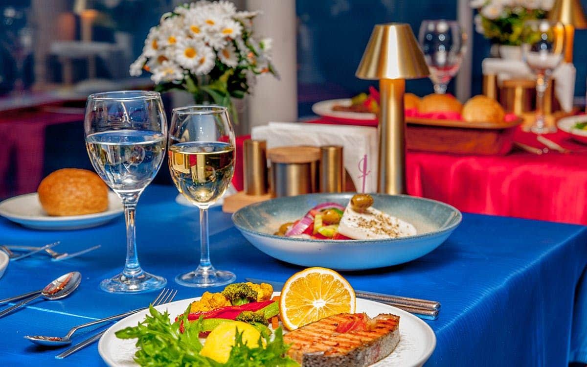 Istanbul: Bosphorus Dinner Cruise with Traditional Dervish Show A table set with wine glasses, grilled salmon, vegetables, and salad. Flowers and a small lamp are in the background.