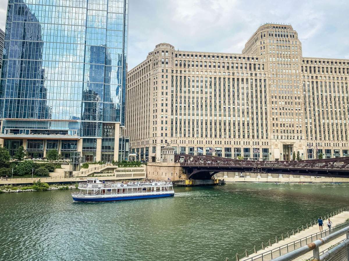 Chicago: Architecture River Cruise from Michigan Avenue Boat on a river beside large buildings, one modern glass, one historic brick, with a bridge in the background.