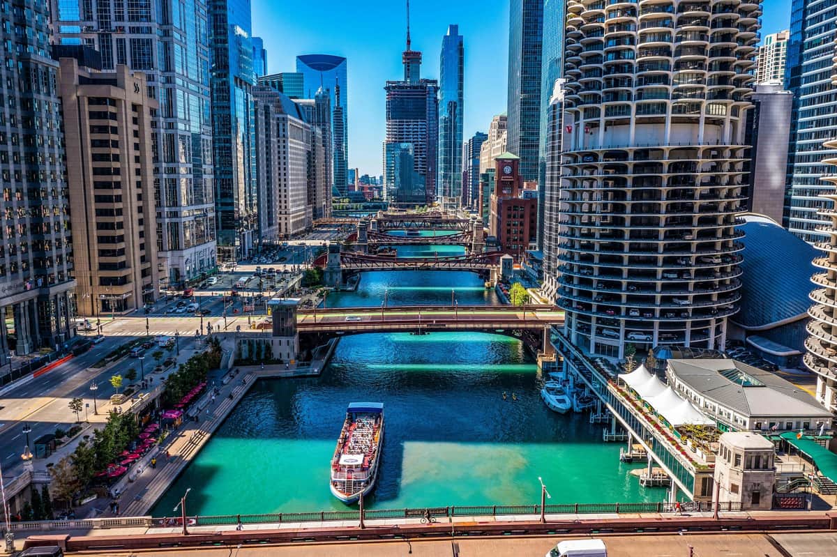 Chicago: Architecture River Cruise from Navy Pier An aerial view of a cityscape with tall buildings, multiple bridges, and a river with a boat carrying people.