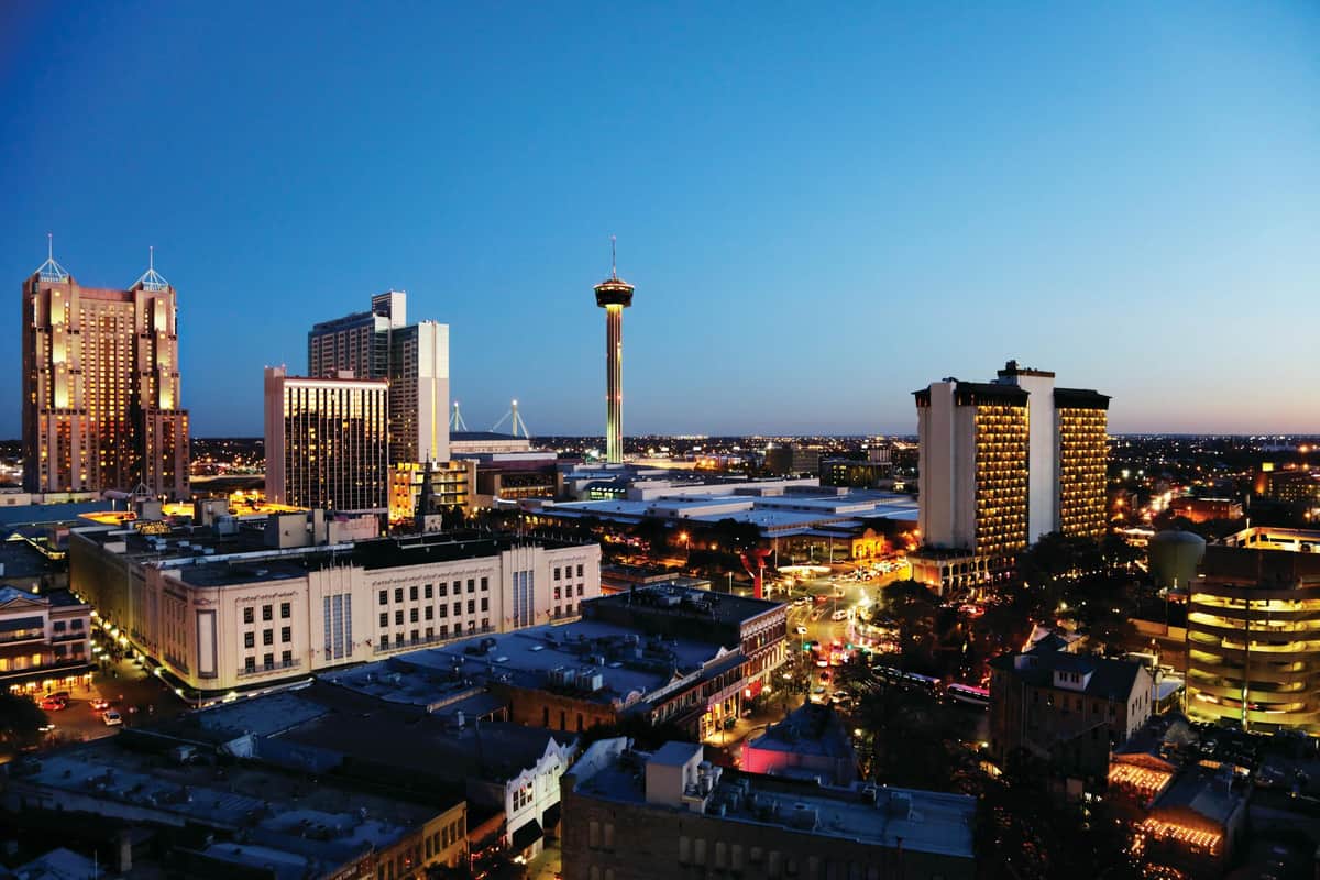 San Antonio : Points forts + visite guidée de l'Alamo Paysage urbain au crépuscule avec de grands bâtiments, une tour proéminente au centre, et des rues éclairées par les lumières des voitures et des bâtiments.