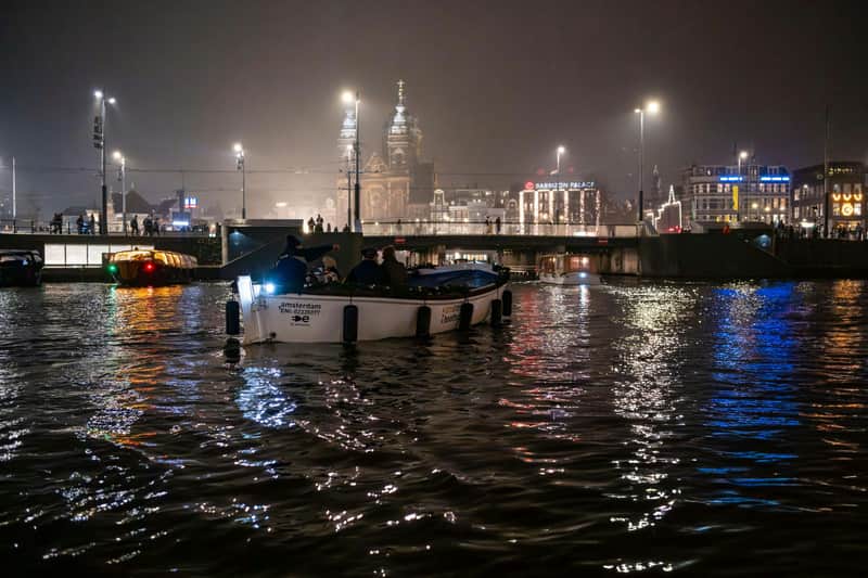 夜晚，一艘船在河上，背景是灯火通明的城市景观和大教堂。