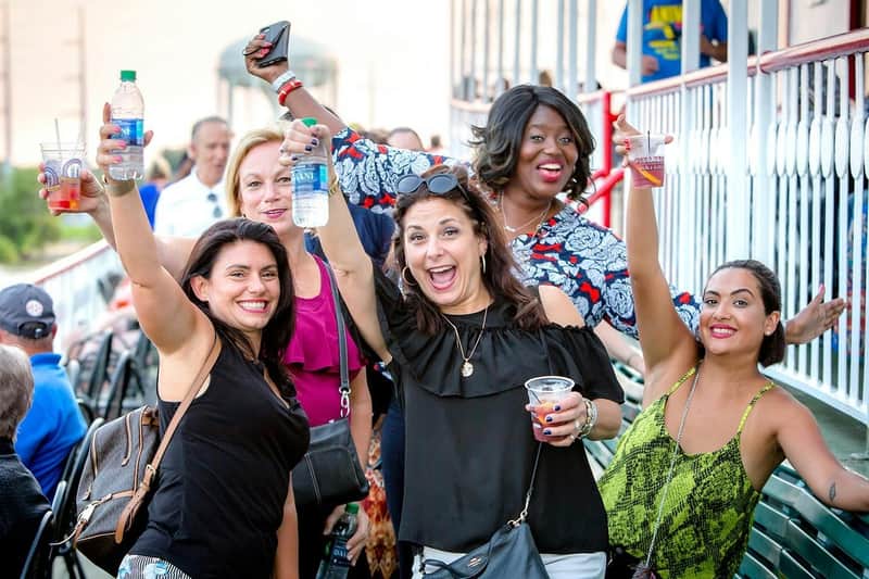 Een groep mensen die glimlacht en feestelijk met hun drankjes proost, buiten met een balustrade op de achtergrond.