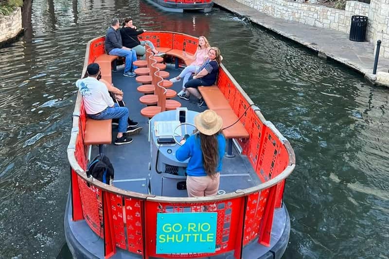 Een rivierpendelboot met passagiers die aan de zijkanten zitten en een gids die vooraan aan het roer staat, met het opschrift ‘GO RIO SHUTTLE’.